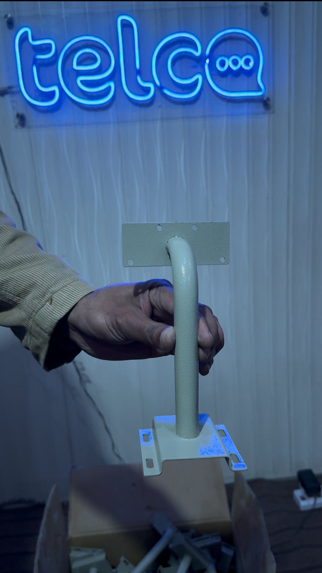 Hand holding a white metal handle with a neon 'telco' sign in the background