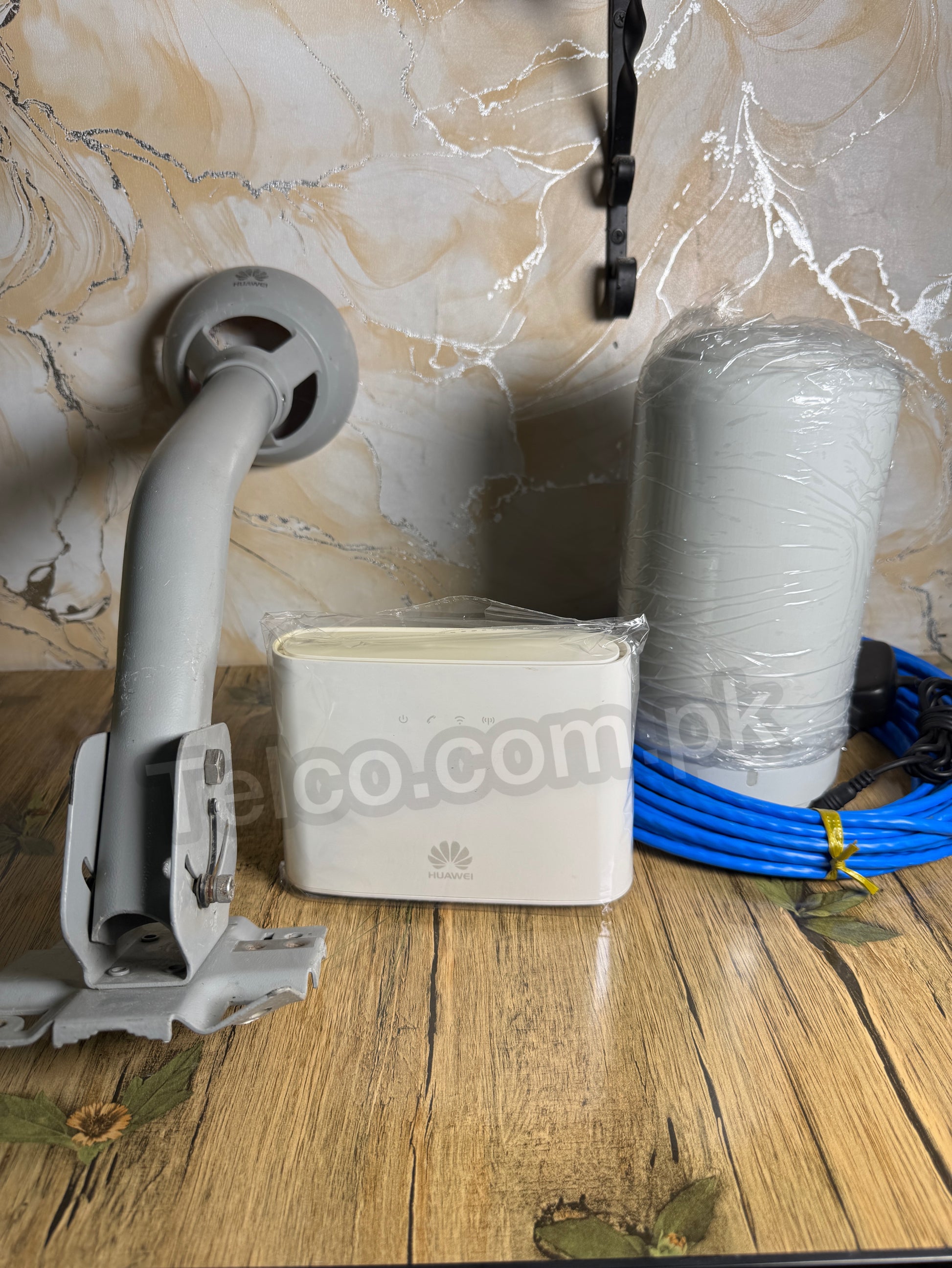 White device with blue cable on a wooden surface against a marble wall.